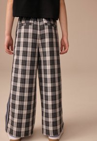 Pantalons larges en écossais noir, blanc et gris avec une texture lisse. Dotés de deux poches arrière et d'un subtil détail de rayure sur le côté.