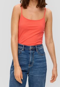 Débardeur corail ajusté avec des bretelles fines, associé à un jean en denim bleu taille haute avec des poches avant et une fermeture à bouton.