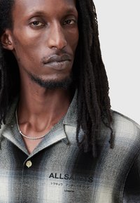 Camisa de manga corta, con cuello, en patrón degradado en blanco y negro. Presenta un cierre de botones, una textura sutil y una marca en el área del pecho.