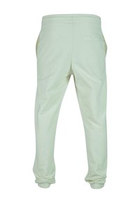 Pantalones de chándal verde claro fabricados en un tejido suave, con cinturilla elástica, bolsillos laterales y un único bolsillo trasero con un detalle de costura.
