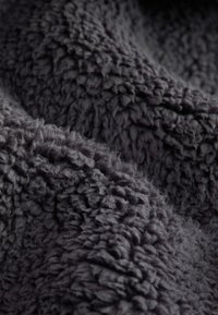 Gestructureerde donkergrijze stof met een pluche, zachte oppervlakte, voorzien van een dicht oppervlak en een oneven patroon door het hele materiaal. Ideaal voor warme toepassingen.