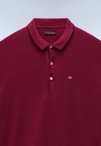 Burgundy színű pólóing klasszikus gallérral, három gombos placket-zel és hímzett norvég zászlóval a bal mellen. Simogató tapintású.