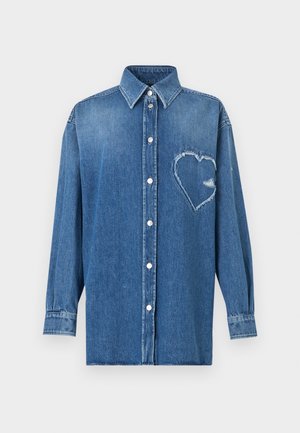 Camisa de mezclilla azul de manga larga con botones, cuello puntiagudo y un parche desgastado en forma de corazón en el pecho izquierdo.