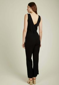 Combinaison noire avec un design au dos en V profond, sans manches, taille cintrée et pantalon large. Fabriquée en tissu doux avec une texture lisse.