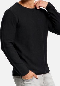 Zwarte lange mouwen trui met een gestructureerd breipatroon, ronde halslijn en geribbelde manchetten, gecombineerd met lichtgrijze jeans.