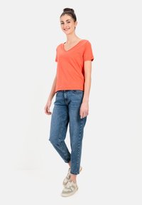 Koralfarvet V-hals t-shirt parret med lyseblå jeans og grå sneakers. T-shirten har korte ærmer og en afslappet pasform.