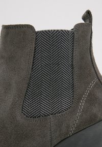 Stivale alla caviglia in camoscio grigio con un pannello elastico nero testurizzato caratterizzato da un motivo a spina di pesce, con cuciture in risalto sui lati.