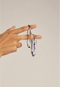 Mehrfarbiger Perlen-Schmuck, der zwischen zwei Fingern gehalten wird. Enthält Perlen in Blau und Schwarz sowie Perlen in verschiedenen Formen und Größen.