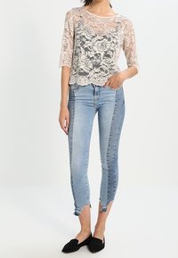 Top in pizzo color nude con motivo floreale, maniche 3/4; abbinato a jeans skinny blu chiaro con orlo strappato e scarpe slip-on nere.