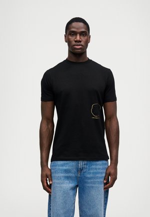 T-shirt en coton noir à manches courtes, avec un design en contour doré sur la poitrine. Associé à un jean légèrement déchiré, bleu clair.