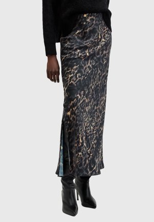 Femme portant une jupe longue à imprimé léopard noir et marron avec une fente latérale, associée à des bottes noires à talons hauts et un pull noir.