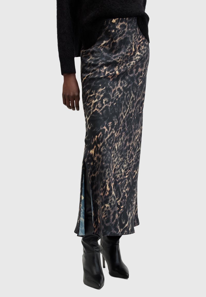 Femme portant une jupe longue à imprimé léopard noir et marron avec une fente latérale, associée à des bottes noires à talons hauts et un pull noir.