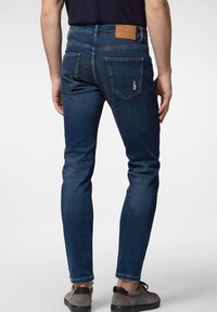 Mörkblå denimjeans med smal passform, med en läderpatch vid midjan och två bakfickor, som visar subtila slitna detaljer.