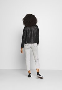Black leather jacket with a fitted design, paired with light gray jeans and black high-top sneakers. Textured finish on the jacket.