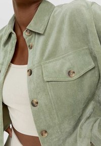 Light green corduroy shirt jacket with a collar, two front pockets, and brown buttons. The texture is ribbed and soft.
