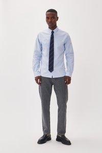 Lichtblauw button-up overhemd met lange mouwen, gecombineerd met grijze jeans en zwarte schoenen. Het overhemd heeft een kraag en een blauw gestreepte stropdas.