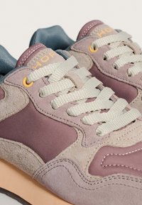 Zapatillas que presentan una combinación de ante rosa claro y malla gris, con cordones crema, acentos texturizados y una suela suave en tono melocotón.