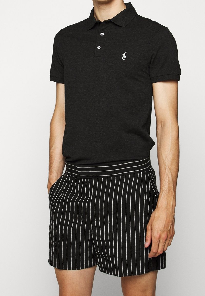 Polo noir avec une patte de boutonnage à trois boutons et un logo blanc, associé à un short noir rayé avec une large ceinture et des poches.