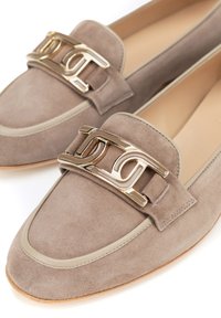 Mocasines de ante beige con un hebilla dorada, que presentan una punta redondeada y un ribete de contraste alrededor de la abertura. Suela plana.