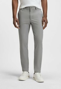 Pantalons de costume gris en matière lisse, avec une coupe classique, des poches avant, et associés à des baskets blanches pour un look décontracté.