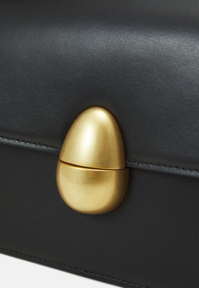 Čierna kožená kabelka s zlatým oválnym uzáverom a hladkým povrchom, s precíznym prešívaním pozdĺž okrajov.