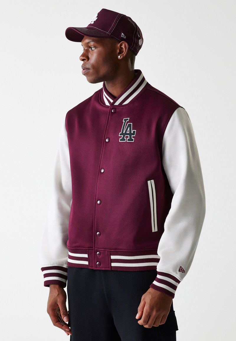 Chaqueta varsity burdeos con mangas de cuero blanco, puños y collar de canalé. Presenta el logo "LA", botones de presión y dos bolsillos laterales.