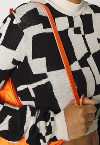 Zwart-crème gebreide trui met lange mouwen, geribbelde manchetten en een hoge hals; met een oranje schoudertas.