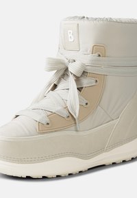 Jasnobeżowy, wysokiego kroju but z teksturowaną tkaniną, wyściełanym kołnierzem i szarymi sznurowadłami. Posiada gumową podeszwę oraz formowane akcenty.