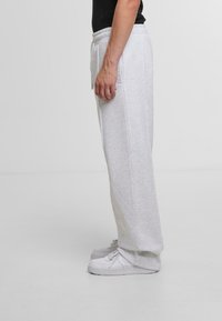 Light grey sweatpants in a relaxed fit, featuring an elastic waistband and two side pockets; paired with white sneakers.