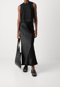 Czarny koronkowy top z wycięciem, ozdobiony złożonymi wzorami kwiatowymi, w połączeniu z czarną satynową spódnicą maxi. Dodatki to czarna torebka i masywne czarne sanda�ły.