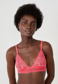 Bralette de encaje rosa con forma triangular, patrón floral, tirantes ajustables y un borde festoneado a lo largo del escote y la banda.