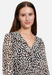 Zwart en crèmekleurig jurk met een V-halslijn, gerimpelde kraag en elastische tailleband, met lange doorschijnende mouwen.