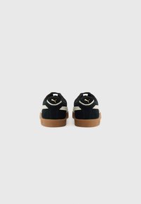 Black suede sneakers with a tan rubber sole, featuring a white stripe and gold logo on the heel. Simple design, low-cut shape.
