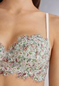 Bloemmotief bralette in wit met roze en groene accenten. Heeft kantafwerking en fijne stiksels langs de randen. Verstelbare bandjes.
