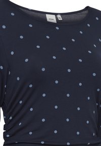 Námořnická modrá blůza s světle modrými puntíky, kulatým výstřihem a detailním nabíráním po stranách. Vyrobeno z jemné, elastické tkaniny.