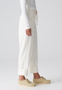 Pantalons en velours côtelé beige clair avec une coupe décontractée, dotés d'une taille élastique, d'un cordon de serrage, de poches latérales et de poignets repliés. Associés à des chaussures beiges.