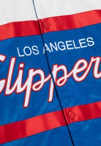Veste en satin bleu avec des accents rouges et blancs. Logos "Los Angeles" et "Clippers" en broderie blanche et rouge. Dispose d'une fermeture à bouton-pression.