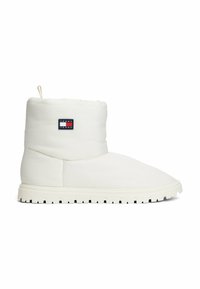 Botín acolchado blanco hasta el tobillo con punta redondeada, suela texturizada y un parche de marca que presenta un logo rojo, blanco y azul en el lateral.