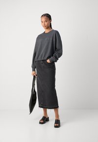 Felpa grigio carbone con logo impresso, abbinata a una gonna maxi in denim nera con orlo strappato e sandali platform neri.