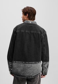 Sort denimjakke med et gradientdesign og en lysere grå bunddel. Klassisk krave, knapmanchetter og løs pasform.