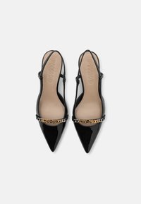 Črne patenten usnjeni polkape s koničastimi nosovi, verižni detajl čez gornji del in bež notranjosti z vtisnjenim logotipom.