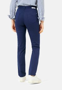 Osoba w dopasowanych granatowych spodniach, białych sneakerach i niebiesko-białej paskowanej koszuli z długim rękawem, stojąca z rękami swobodnie przy boku.