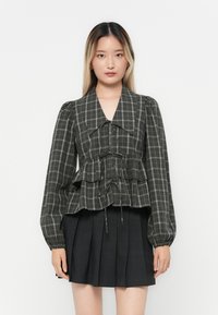 Dark plaid blouse with puffed sleeves, peplum waist, and drawstring detail, paired with a black pleated skirt.
