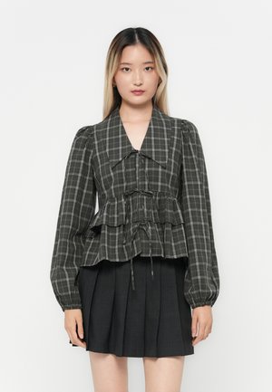 Dark plaid blouse with puffed sleeves, peplum waist, and drawstring detail, paired with a black pleated skirt.