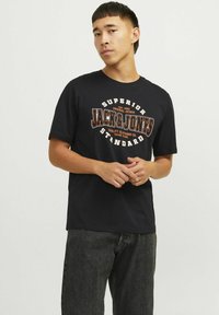 Sort bomulds t-shirt med rund halsudskæring og korte ærmer, der har et grafisk print i orange og hvid med teksten "JACK & JONES STANDARD."