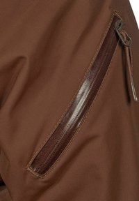 Brunt tyg med en dragkedja, där dragkedjan har ett släta, mörkbrunt draghandtag. Materialet har en matt textur och en subtil lyster.