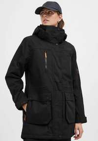 Wasserdichte schwarze Parkajacke mit hohem Kragen, mehreren Taschen und einem mit Reißverschluss versehenen Front. Verfügt über kontrastierende braune Akzente und verstellbare Bündchen.