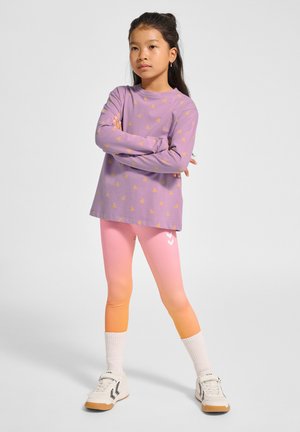 Paarse langemouw shirt met een geel driehoekpatroon, gecombineerd met ombre roze tot oranje leggings met witte chevronaccenten. Witte sneakers en sokken.