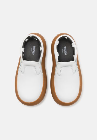 Des chaussures blanches à enfiler avec une semelle en caoutchouc brun texturé, présentant un motif à pois noir et blanc à l'intérieur.