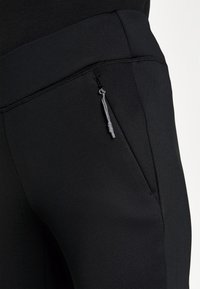 Černé sportovní kalhoty s elegantním designem, hladkým povrchem a kapsou na zip s kovovým úchytem pro bezpečné uložení.